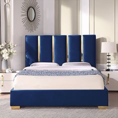 a bed with blue headboard and white sheets in a living room next to a mirror