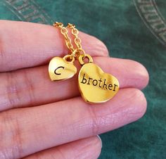 a person holding two heart shaped pendants with the word brother written on one of them