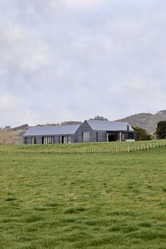 a house in the middle of a large field with grass on both sides and mountains in the background