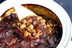 a pot filled with beans and sauce on top of a table next to a wooden spoon