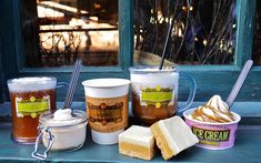 there are many different types of ice creams on the window sill with cups and spoons next to them