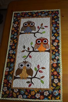 two owls sitting on a tree branch with leaves and flowers in the background, one is made from quilts