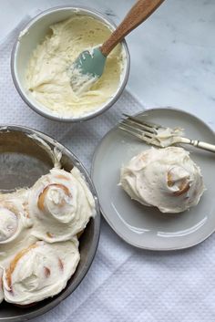 two bowls filled with whipped cream on top of a white table cloth next to silverware