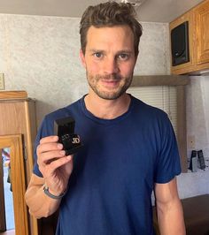 a man holding up a small black object in his right hand and smiling at the camera