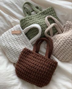 four crocheted purses on a bed with white sheets and brown tags hanging from the handles