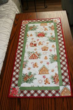 a christmas table runner with gingerbread houses and trees on it, sitting on top of a wooden table