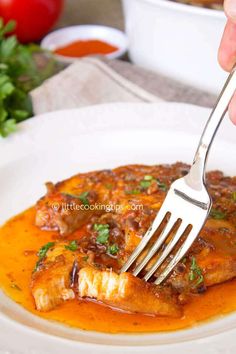 a person is holding a fork over some food on a white plate with tomatoes and parsley