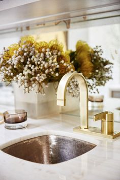 a sink with a gold faucet and some flowers in the vase next to it