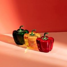 three colorful peppers sitting on top of a white counter next to a red and orange wall