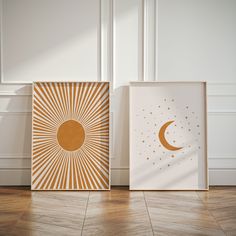 two framed art prints on the floor in front of a white wall with gold stars and a half moon