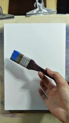 a person holding a paintbrush in their left hand and painting on a piece of paper