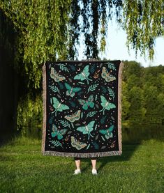 a woman standing in the grass holding up a black blanket with green butterflies on it