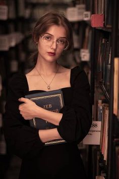 a woman standing in front of a bookshelf with her arms crossed and looking at the camera