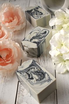 three soap bars sitting on top of a white wooden table next to pink and white flowers