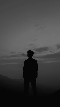 a man standing on top of a hill under a dark sky with clouds in the background