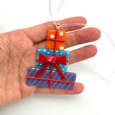 a hand holding an ornament shaped like a gift box with red, orange and blue bows