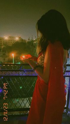 a woman standing on a balcony looking at her cell phone with the city lights in the background