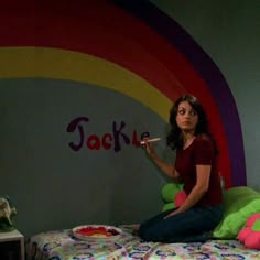 a woman sitting on top of a bed in front of a rainbow painted wall