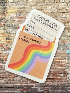 a ticket sitting on top of a brick wall next to a rainbow painted sign that says support your local library