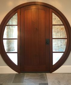 a circular wooden door with two windows in the center and an arched glass window above it