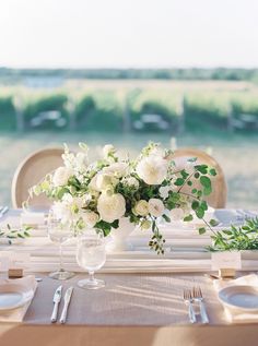 a table set with white flowers and greenery for an elegant wedding reception at the vineyard