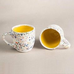 two coffee mugs sitting side by side, one with yellow inside and the other has sprinkles on it