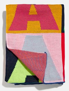 a multicolored blanket is folded on top of a white surface with black, yellow, pink, and green squares