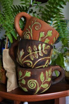 two brown and green cups sitting on top of a wooden table next to some plants