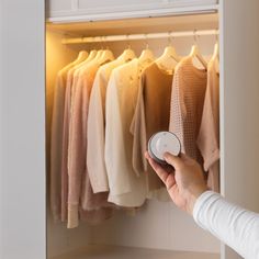 a person is holding an electronic device in front of a closet full of shirts and sweaters