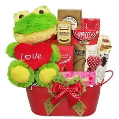 a stuffed frog sitting in a red bucket filled with chocolates, candy and treats