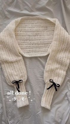 a white knitted sweater with black bows on the collar and sleeves, sitting on top of a bed