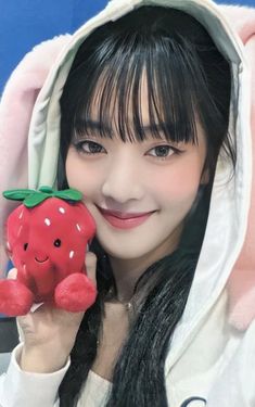 a girl in a white hoodie holding up a red stuffed animal toy with a smile on it's face