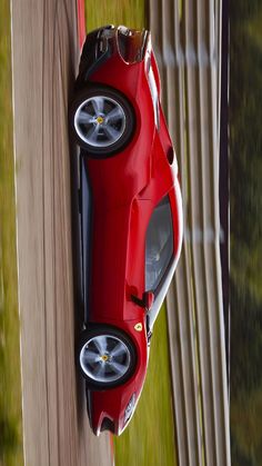 a red sports car driving down a road next to a wooden fence and grass area