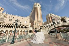 a bride and groom kissing in front of a large building with a bridge over it