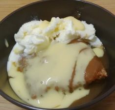 a black bowl filled with mashed potatoes and meat covered in gravy on top of a wooden table