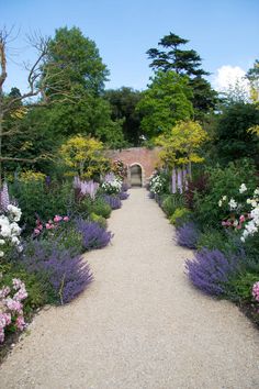 a pathway lined with lots of flowers and trees in the middle of a park area