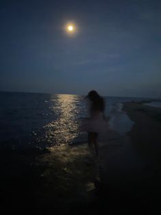 a woman standing on top of a beach under a full moon at the ocean's edge