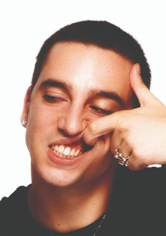 a young man smiles as he puts his hand on his nose and fingers to his forehead