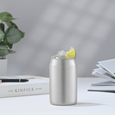 a silver can with a lemon wedge in it sitting on a table next to some books