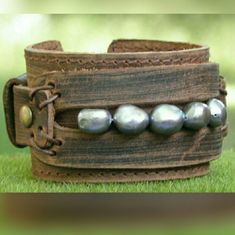 a leather bracelet with metal beads on top of it in the middle of some grass