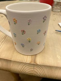 a white coffee cup sitting on top of a wooden table with flowers painted on it