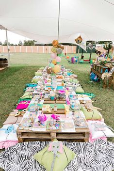 a long table covered in lots of items on top of a lush green field next to a white tent