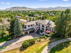 an aerial view of a home in the hills with mountains in the background and trees surrounding it