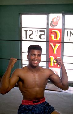 a shirtless man posing for a photo in front of a gym sign and window