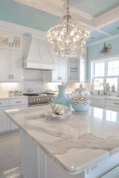 a white kitchen with marble counter tops and chandelier hanging from the center island