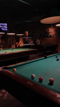 people are playing pool in a dimly lit room with billiards on the tables