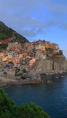 a small village on top of a hill next to the ocean with boats in the water