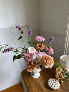 a wooden table topped with flowers next to a vase filled with pink and white flowers