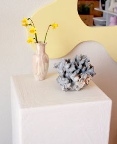 a vase with yellow flowers sitting on top of a white table next to a mirror