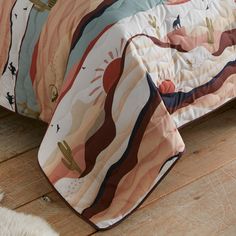 a bed covered in a colorful comforter next to a white rug on top of a wooden floor